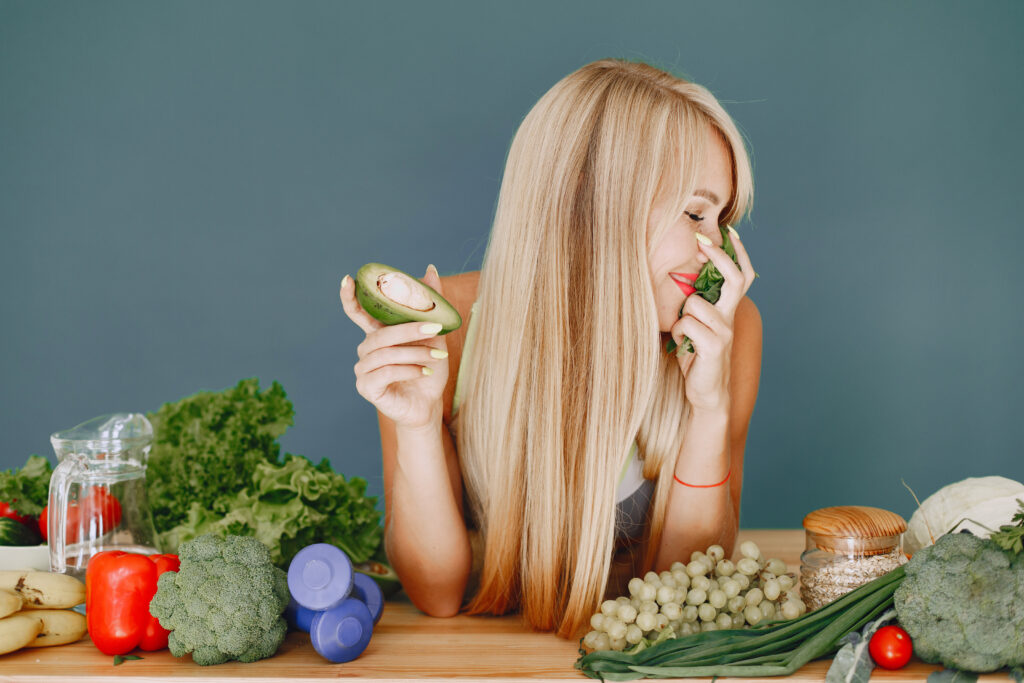 Remedios naturales y alimentación para un cabello saludable. hermosa chica hace una ensalada rubia deportiva en una cocina mujer con aguacate